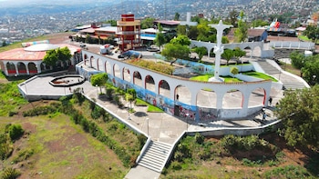 Vista aérea de un complejo turístico con la torre Mirador Acuchimay, la escultura de Cristo, una gran cruz, arcos con murales, edificios y una ciudad al fondo