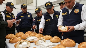 Agentes del INPE inspeccionan panes que contienen paquetes de droga sobre una mesa blanca. Uno de los agentes sostiene medio pan con un bulto blanco.