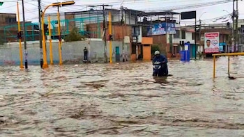 Una calle cubierta por agua turbia, una persona en motocicleta en el centro, postes con semáforos amarillos y fachadas de edificios