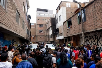 Calle con edificios de ladrillo. Multitud de personas y policías, dos camionetas, cinta amarilla y un edificio con fachada ennegrecida