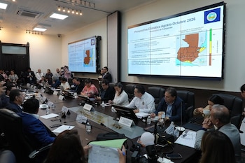 Personas sentadas alrededor de una mesa de reuniones frente a pantallas que proyectan gráficos y un mapa de Guatemala