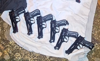 Una escopeta, un subfusil, dos pistolas, cargadores y diversos cartuchos y balas ordenados sobre una mesa de madera