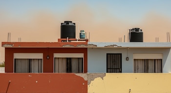 Dos viviendas de concreto con techos planos, tinacos negros, tanque de gas y ventanas con persianas. Las fachadas muestran pintura pelada en terracota, azul y amarillo.