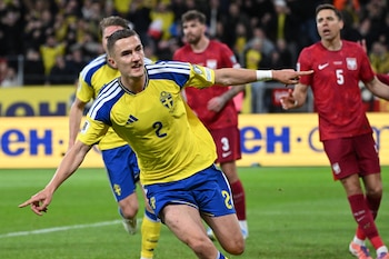 Jugador sueco con camiseta amarilla número 2 celebra en un campo de fútbol verde, brazos extendidos, manos apuntando. Jugadores polacos y público borroso al fondo