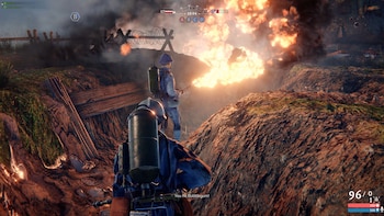Vista de un videojuego que muestra dos soldados en una trinchera con lanzallamas y fuego, alambre de púas, hierba y elementos de interfaz de usuario