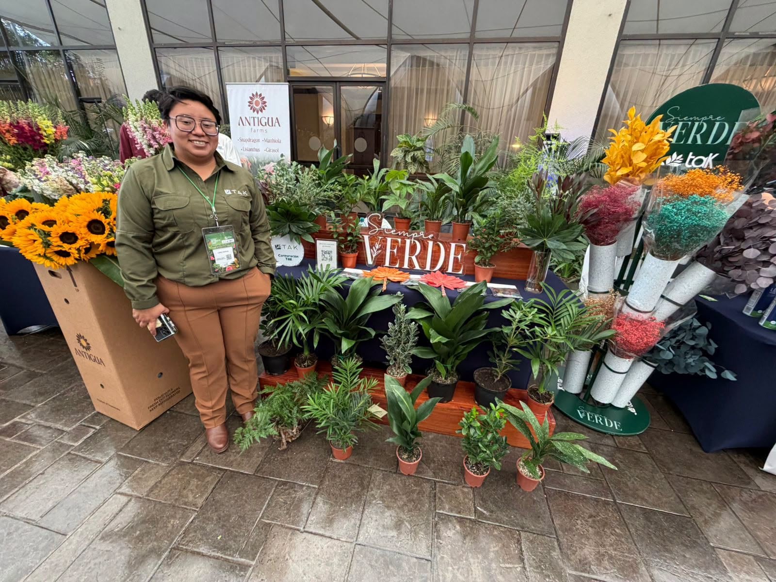 Una expositora presenta una variedad de plantas de interior y arreglos florales en un estand comercial de floricultura. (Agexport Guatemala)