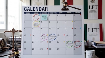 Calendario de pared con fechas marcadas, un post-it azul, balanza de la justicia, un mazo, dos banners y una taza con el logo LFT de México.