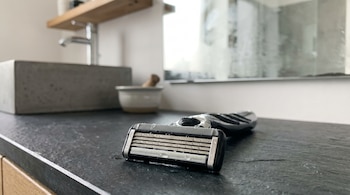 Primer plano de un rastrillo de hombre con múltiples navajas y gotas de agua, apoyado en una encimera oscura en un baño moderno.