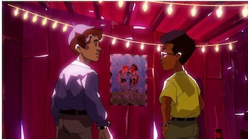 Dos jóvenes de perfil en una habitación con paredes rojas, una guirnalda de luces en el techo y un cartel infantil en la pared