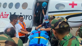 Varios sanitarios y uniformados introducen a una persona en camilla en un avión médico blanco con una cruz roja en el fuselaje