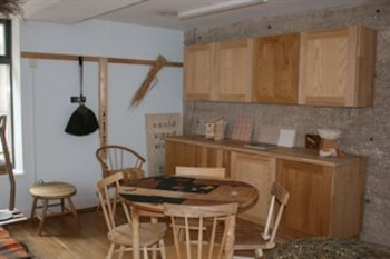 Un espacio interior con una mesa redonda de madera, cuatro sillas, gabinetes en la pared y repisas sobre paredes de textura rugosa