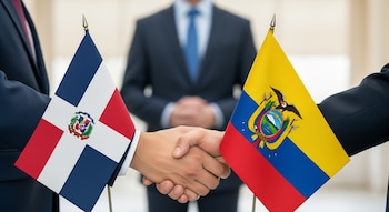 Dos personas con traje estrechan sus manos. Las banderas de República Dominicana y Ecuador están en el primer plano. Otra persona en traje se ve desenfocada al fondo.
