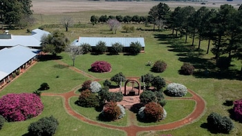 Vista aérea de un campus con edificios de tejados grises, césped verde, senderos y arbustos floridos. Un monumento circular con un arco de ladrillo está en el centro