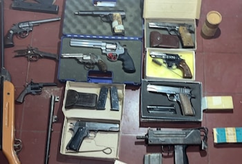 Varias pistolas, revólveres, un subfusil, cargadores y cajas de munición dispuestas sobre un piso de baldosas rojas