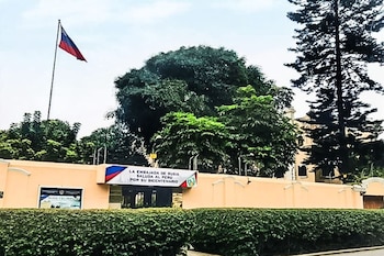 Vista exterior de la Embajada de Rusia con la bandera rusa ondeando. Un banner saluda a Perú por su Bicentenario. Hay un muro claro y un seto verde