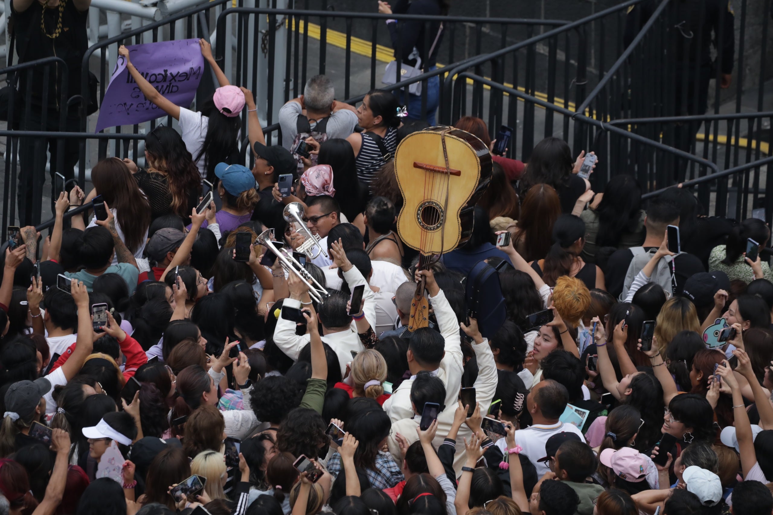 Miles de seguidores de BTS, conocidos como ARMY, se congregan con entusiasmo en el Zócalo de la Ciudad de México, alzando sus teléfonos para capturar el momento en que la banda saluda desde el balcón del Palacio Nacional. (Jefatura CDMX)