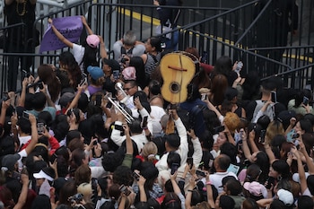 Una multitud densa de personas sostiene teléfonos móviles en alto, filmando un evento. Se ven barreras metálicas, un trompetista y una guitarra tradicional entre la gente