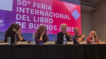 Cinco panelistas, tres mujeres y dos hombres, sentados en una mesa con micrófonos y vasos de agua, frente a una pantalla de la Feria del Libro.