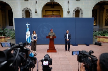 Un monitor de pantalla plana muestra a un hombre sentado tras un escritorio, rodeado por personas y cámaras de televisión