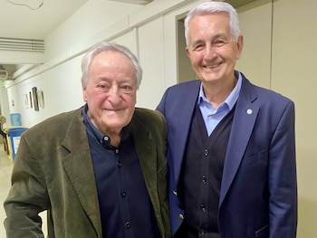 Dos hombres, Roberto Carnaghi y Ricardo Antoniassi, posan sonriendo frente a una pared clara en un pasillo interior