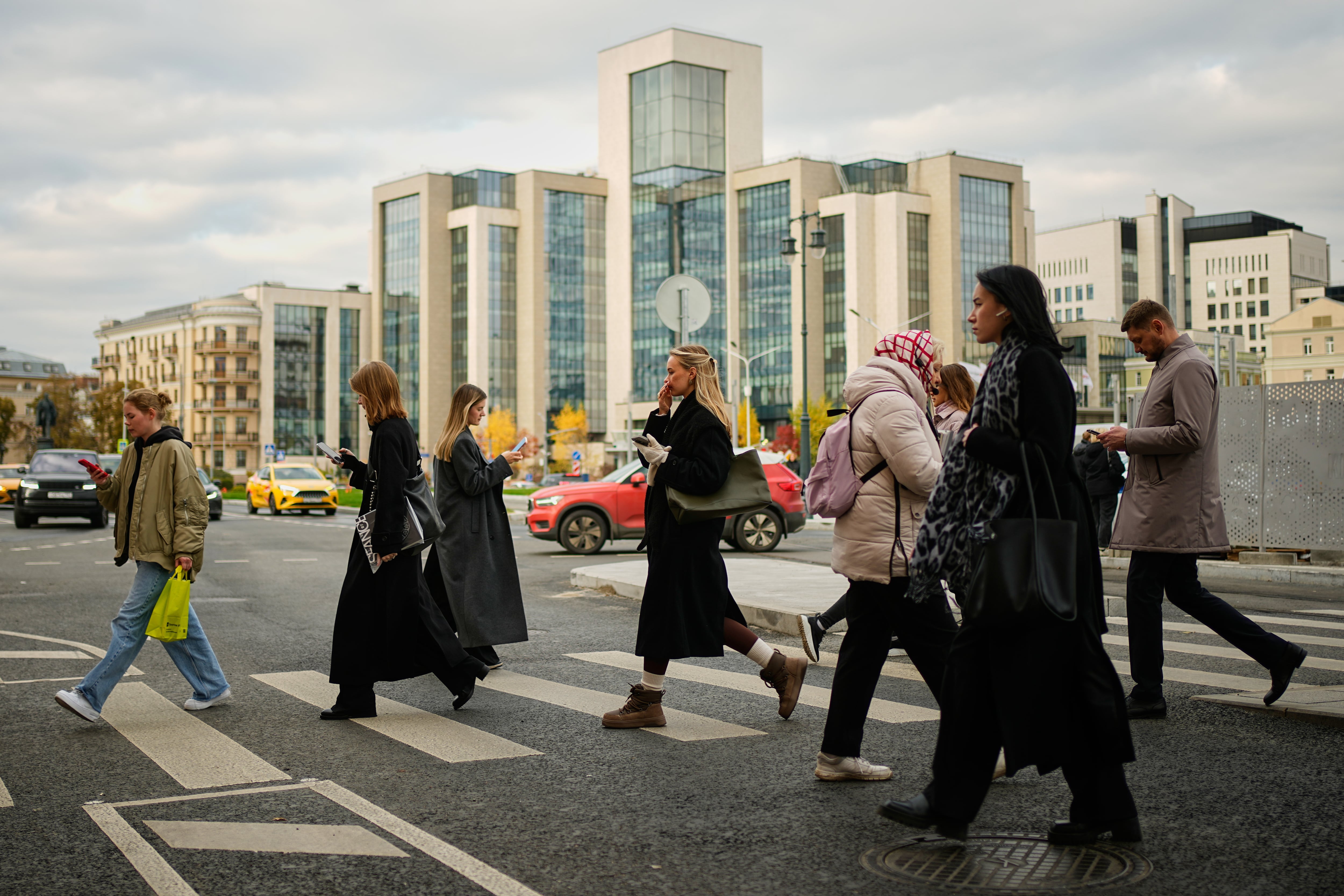 Gente cruzando una calle con la sede de la compañía petrolera rusa Lukoil al fondo, en Moscú, Rusia, el jueves 23 de octubre de 2025(AP Foto/Pavel Bednyakov)