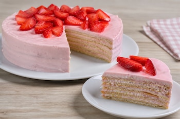 Carlota redonda con crema rosa y trozos de fresas en la parte superior, sobre un plato blanco con una rebanada al lado.