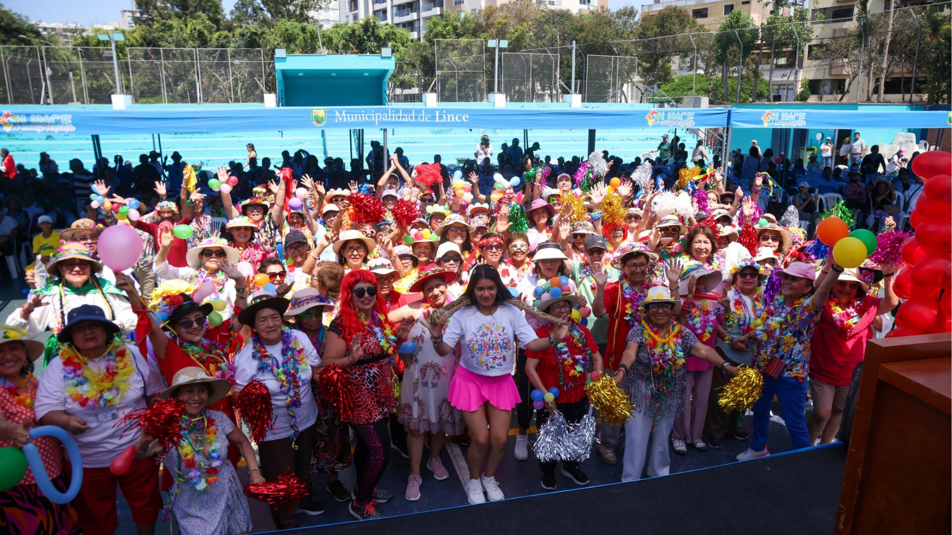 Un grupo numeroso de adultos mayores de Lince celebra con alegría la renovación de sus votos matrimoniales por San Valentín, vistiendo trajes festivos y coloridos bajo el sol.