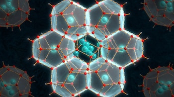 Visualización 3D de una estructura de clatrato. Jaulas poliédricas translúcidas de color azul claro con átomos rojos y grises, encapsulan esferas azules en su interior.