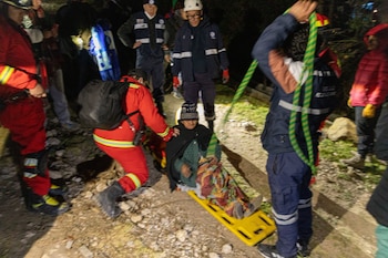 Rescatistas trasladan a una mujer con mantas en camilla amarilla. Se observan varias personas uniformadas, terreno rocoso y poca iluminación nocturna