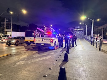Una patrulla de policía con luces encendidas y varios agentes parados de noche junto al acceso a una estación de transporte público