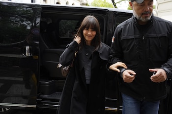 Aitana viste un abrigo negro y camina tomada del brazo de un hombre con chaqueta negra junto a una camioneta oscura