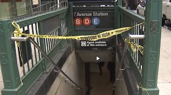 Entrada a las escaleras de la estación de metro 7 Avenue con barandillas verdes y una cinta amarilla que bloquea el paso