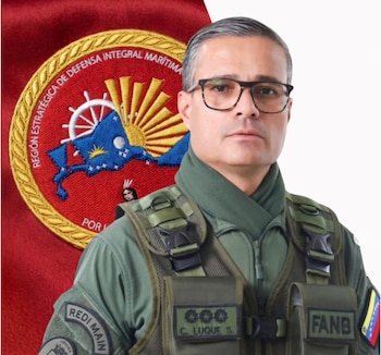 Retrato de hombre con gafas, uniforme militar verde, chaleco táctico, parches "REDI MAIN", "FANB", "C. LUQUE S." y bandera de Venezuela. Fondo rojo con emblema naval