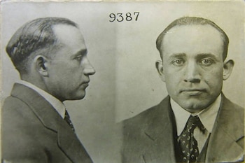 Fotografía en blanco y negro de un hombre de perfil y de frente vestido con traje y corbata, con el número 9387 impreso en la parte superior
