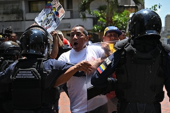 Un hombre con camiseta blanca grita y empuja un escudo policial, frente a dos oficiales de la Policía Nacional Bolivariana en equipo antidisturbios