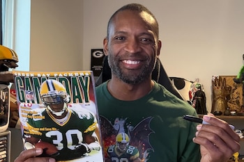 Un hombre sonriente de piel oscura, con barba, sostiene una revista y un marcador negro