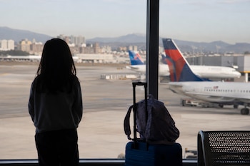 Una menor observa la pista de un aeropuerto junto a una maleta (Imagen Ilustrativa Infobae)
