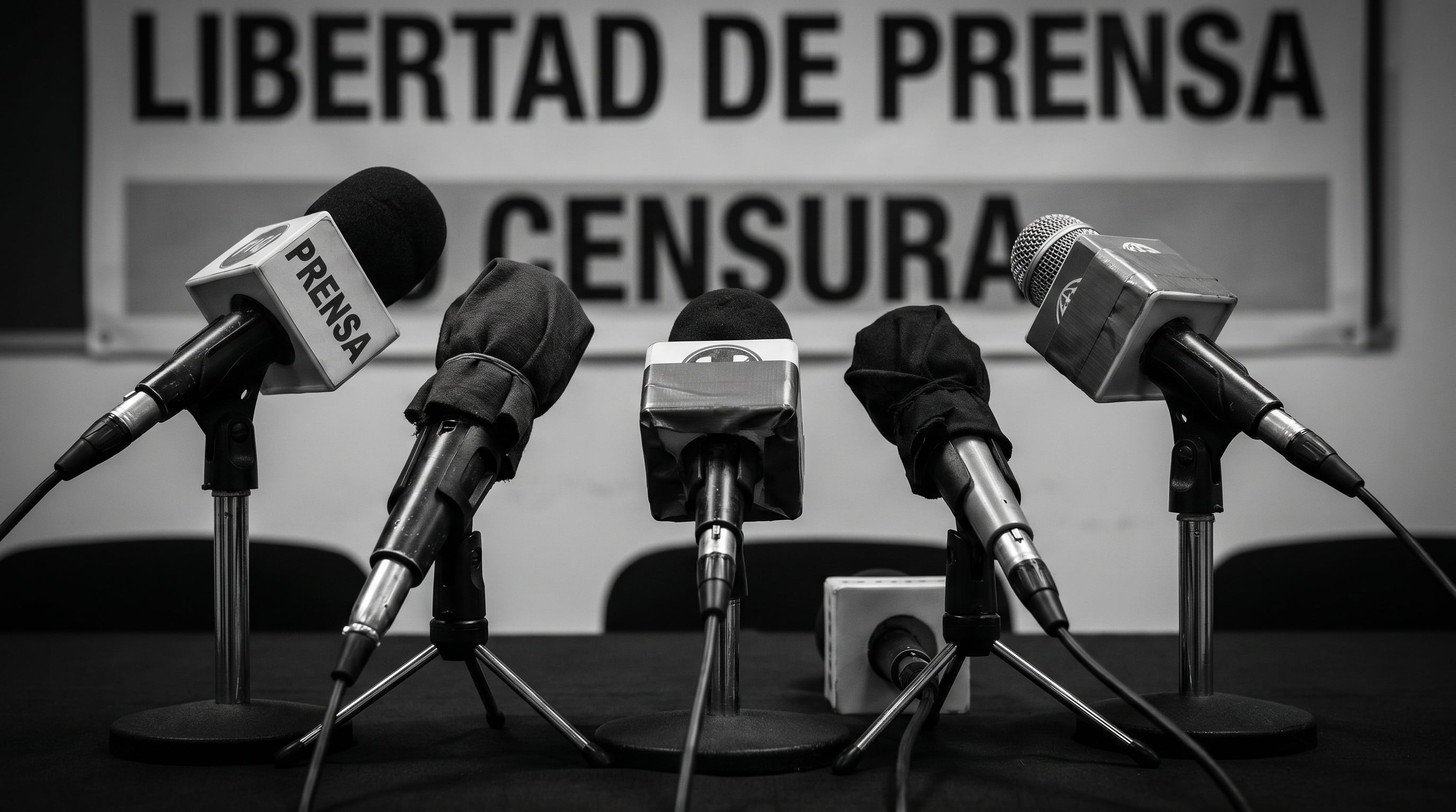 Micrófonos, algunos cubiertos, ante un cartel que dice