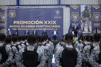 Filas de agentes en uniforme camuflado escuchan a un orador en un escenario con un gran letrero del Sistema Penitenciario de Guatemala