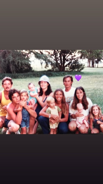 Una fotografía de un grupo familiar numeroso compuesto por adultos, niños y bebés sentados en el césped de un parque al aire libre