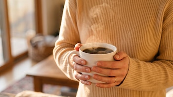 Manos de una persona sostienen una taza blanca con café humeante