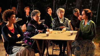 Personas sentadas a la mesa con vasos de plástico en un espacio al aire libre durante la noche con árboles al fondo