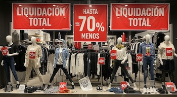 Escaparate de tienda de ropa con varios maniquíes vistiendo prendas, carteles de "Liquidación Total" y "Hasta 70% Menos", y un letrero de "Sold Out".