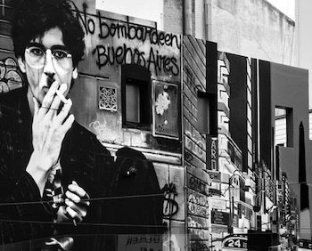 Pared con un mural en blanco y negro que muestra a un hombre con gafas que fuma un cigarrillo y el texto manuscrito No bombardeen Buenos Aires