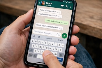 Primer plano de una mano sosteniendo un celular con la pantalla mostrando un chat de WhatsApp y el teclado, donde el pulgar presiona la barra espaciadora.