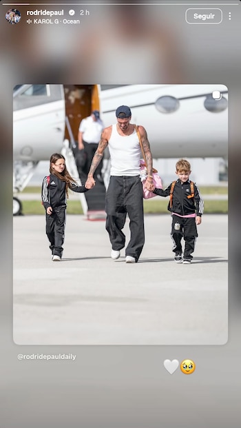Un hombre, una niña y un niño caminan de la mano sobre una pista de aeropuerto. La parte delantera de un avión privado y una persona borrosa se ven al fondo