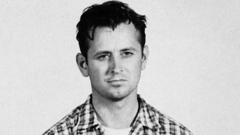 Fotografía en blanco y negro de un hombre blanco con el pelo oscuro y rizado, y una camisa de cuadros, mirando al frente con expresión seria