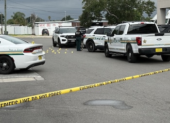 Tres vehículos de la oficina del Sheriff de Polk, un oficial, marcadores de evidencia amarillos y cinta de "Crime Scene Do Not Cross" en una calle