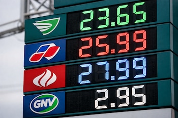 Panel digital con precios de combustible iluminados en LED: 23.65 (verde), 25.99 (rojo), 27.99 (azul), 2.95 (blanco), y logos de marcas a la izquierda.