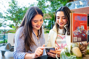 Dos mujeres miran la pantalla de un teléfono inteligente que una de ellas sostiene con la mano en un espacio exterior